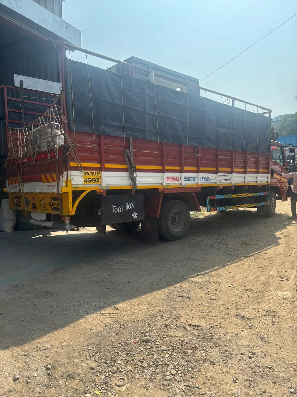 Red high-side goods truck with black tarpaulin covering the upper cargo body