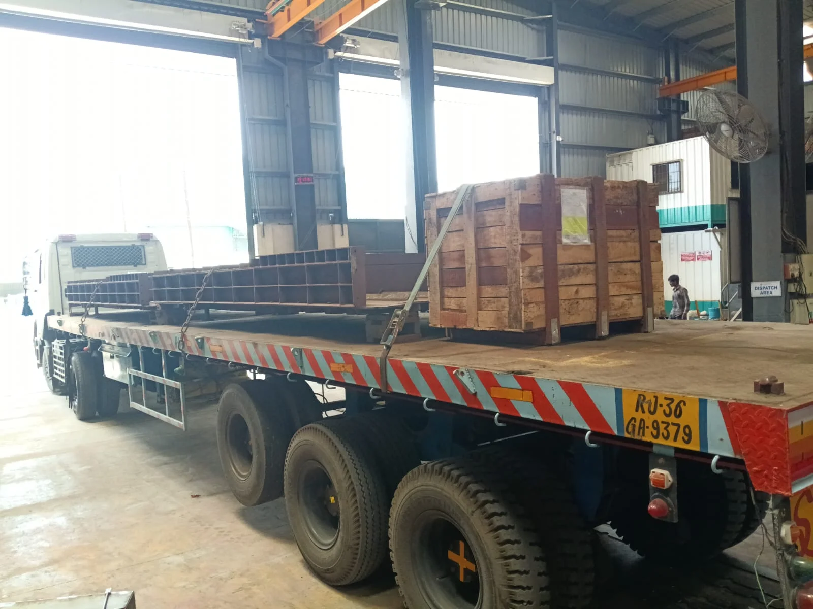 Flatbed truck carrying a wooden machinery crate and steel structure inside a factory