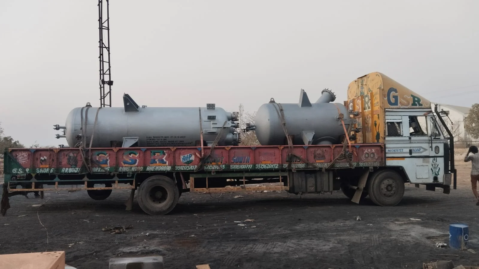 Open-body goods truck carrying cylindrical industrial vessels secured with straps