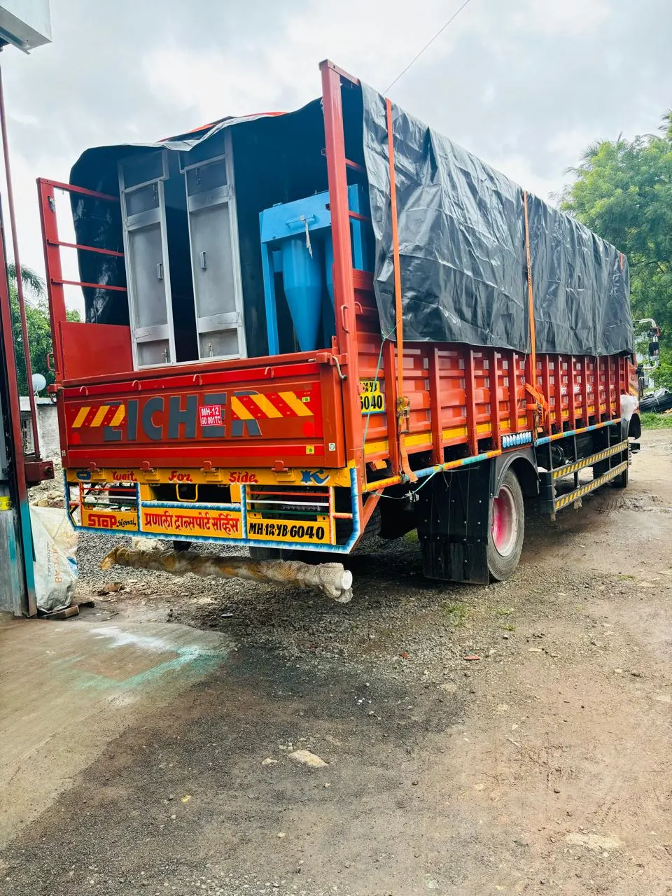 Red open-body goods truck loaded with cargo and covered with a black tarpaulin